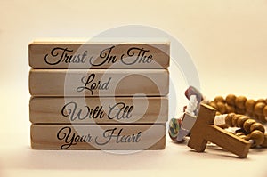 Trusting God message text on wooden blocks with Holy Rosary background.