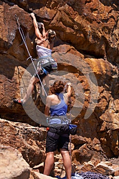 She trusts her belaying partner wholeheartedly. A woman climbing up a rock face while her belayer stands at the bottom.