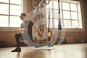 TRX Training. Young athletic man in sports clothing training legs with trx fitness straps in the gym