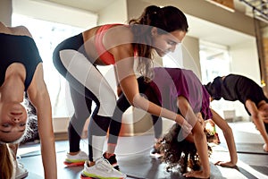 Try Better. Portrait of female trainer helping girl while kids are practising yoga by bending backwards on mats in gym