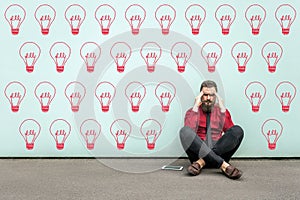 Try to find idea or problem solving. Young thoughtful bearded business man in red shirt sitting on floor and thinking what to do