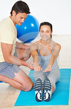 Try to touch your toes. A fitness instructor showing a young woman how to do an exercise.