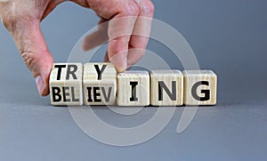 Trying and believing symbol. Businessman turns wooden cubes and changes the word Believing to Trying. Beautiful grey table grey