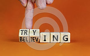 Trying and believing symbol. Businessman turns wooden cubes and changes the word Believing to Trying. Beautiful orange table