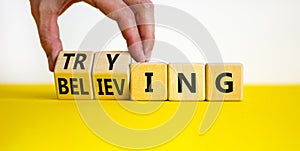 Trying and believing symbol. Businessman turns wooden cubes and changes the word Believing to Trying. Beautiful yellow table white