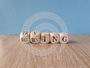 Trying and believing symbol. Turned wooden cubes and changes the word Believing to Trying. Beautiful wooden table blue background