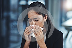 Trying her best to keep the sniffles at bay. a young businesswoman blowing her nose in an office.