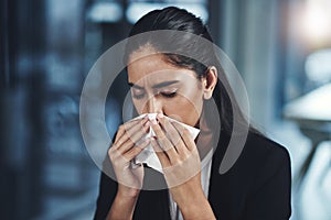 Trying her best to keep the sniffles at bay. a young businesswoman blowing her nose in an office. photo