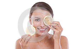Trying a new citrus treatment. Portrait of a beautiful young woman holding a slice of lemon over her eye.