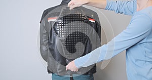 Trying on a plastic back protector for a motorcycle jacket. A girl puts a stove on the back of a biker dressed in a