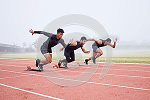 Trying to gain the upper hand. Full length shot of three handsome young male athletes starting their race on a track.