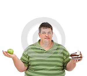 Trying to keep the balance. A obese young man holding an apple in one hand and a slice of cake in the other and looking