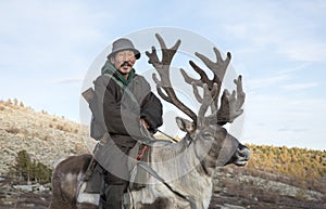 tsaatan man, dressed in a traditional deel, riding his reindeers