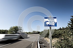 A tsunami warning sign along a coastal highway with a blurred car passing by near the Oregon coast.