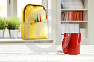 Ttable top with empty space for products or decoration, yellow schoolbag, red mug, blurred spring outside the window background.