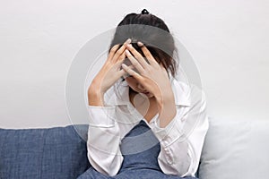 Ttired stressed young Asian woman covering face with hands in living room.