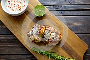 TTwo shrimp cakes on a cutting board with a lemon garlic dipping sauces lemon wedge and a stem or rosemary on a wooden table..