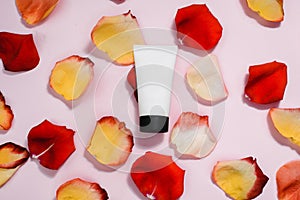 Tuba with moisturizer on a pink pastel background among red, orange rose petals. The concept of skin care, anti-aging care,