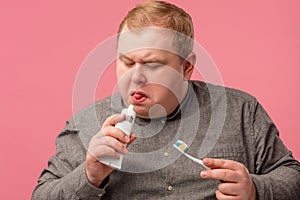 Tubby middle-aged man in grey shirt tastes a new toothpaste that smells strange.