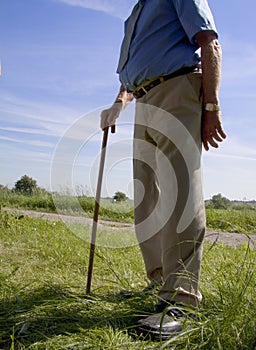 Tubby old man with walking stick in the countryside with grass and a blue sky in the background photo
