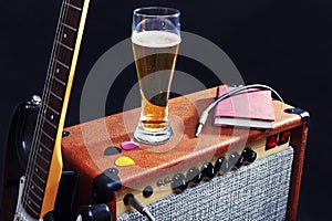 Tube amplifier for electric guitar with black guitar, glass of beer and notepad on black background