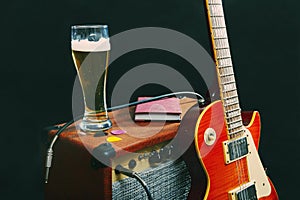Tube combo for guitar with guitar, glass of beer and notepad on black background. Gently toned