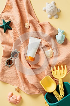 Tube of sunscreen cream, children's sunglasses and beach toys on beige table