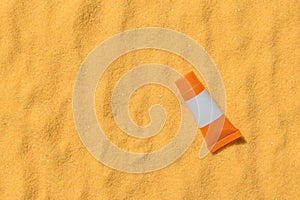 A tube of sunscreen on the sand in the bright rays of the sun