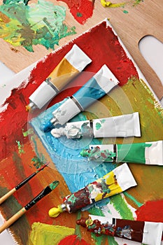 Tubes of colorful oil paints, brushes and canvas with abstract painting on table, flat lay