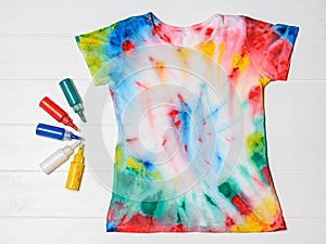 Tubes of paint for clothes and t-shirt in tie dye style on a white table. Flat lay.