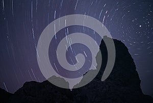 A tufa silhouette at night, backlit by star trails circling the North Star