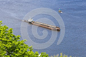 A tug boat hauls a large, empty barge down wide Dnipro river dirung sunny day. Seafaring, navigation on river