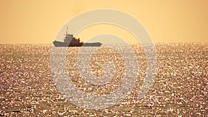 Tug boat in open calm sea, heading back to port at sunset, helps large container ships maneuver. Aerial view, maritime