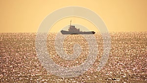 Tug boat in open calm sea, heading back to port at sunset, helps large container ships maneuver. Aerial view, maritime