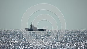 Tug boat in open calm sea, heading back to port at sunset, helps large container ships maneuver. Aerial view, maritime