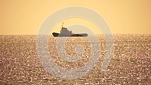 Tug boat in open calm sea, heading back to port at sunset, helps large container ships maneuver. Aerial view, maritime