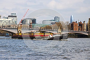 Tug boat pulling a container barge down the River Thames near Westminster bridge with city skyline