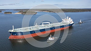 Tug boats escorting large crude oil carrier through narrow Finnish archipelago. Aerial side view