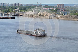 The tug transports a barge loaded with sand along the river.