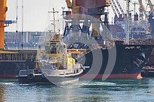 Tugboat at the bow of cargo ship , assisting the vessel to maneuver