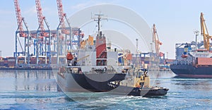 Tugboat at the bow of cargo ship , assisting the vessel to maneuver in Sea Port
