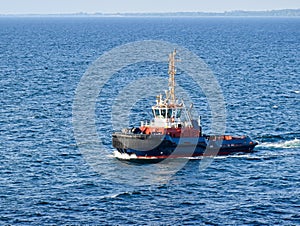 A tugboat navigates on the sea, in the background the coast can be seen