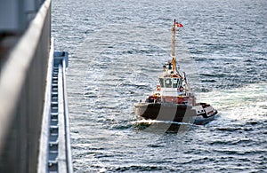 A tugboat navigates on the sea to assista cruise ship entering the port