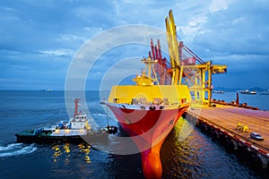 Tugboat push large cargo vessel to berth at port terminal. Port terminal operations and handling equipment