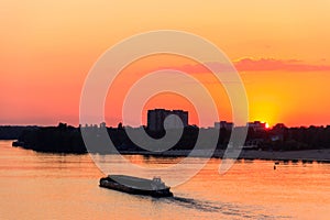 Tugboat pushing heavy long barge on the river Dnieper at sunset