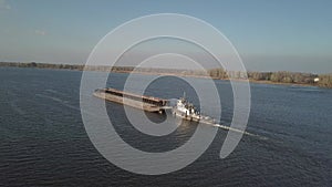 A tugboat ship pushes a barge upstream of the river to transport bulk materials. Aerial photography with a quadcopter or