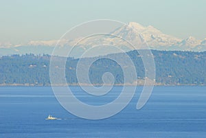 A tugboat traverses and ocean pathway with the San Juan Islands and the beautiful Mount Baker in behind