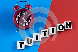 TUITION - word on wooden cubes on a multi-colored background with an alarm clock