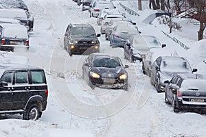 Two cars drive through a snowy yard between rows of parked cars in deep snow in Tula, Russia.