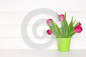 Tulip flower bouquet in bucket on wood table near white wooden board wall. Copy space. Spring rustic background